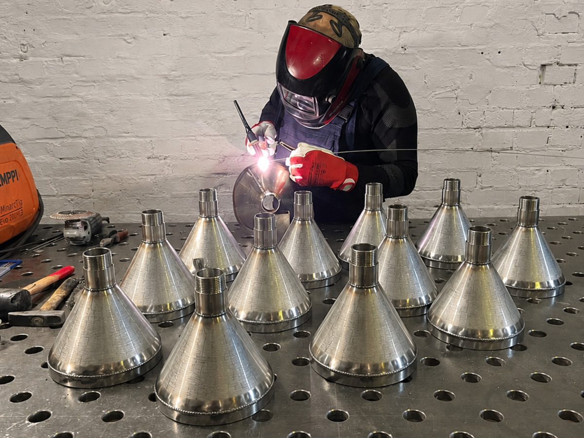 Welder TIG-welding stainless-steel funnels at the welding table